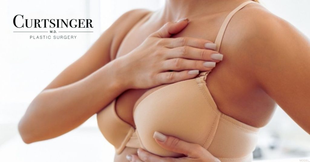 Woman wearing a beige bra is holding her chest (model) Dr. Luke Curtsinger Logo