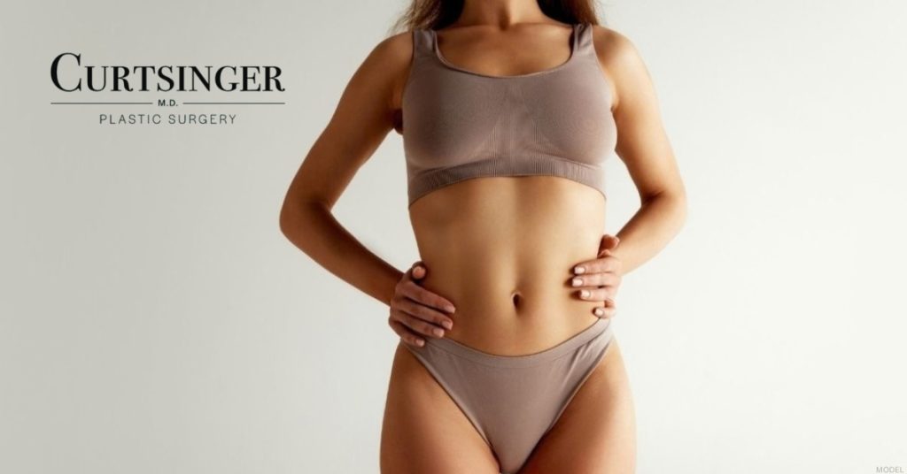 Woman in a sports bra and underwear with her hands on her hips, representing potential mommy makeover results (model) Curtsinger, MD, Plastic Surgery Logo